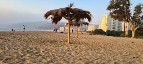 a straw umbrella on a beach with buildings in the background at Departamento en Papudo con acceso directo a la playa in Papudo