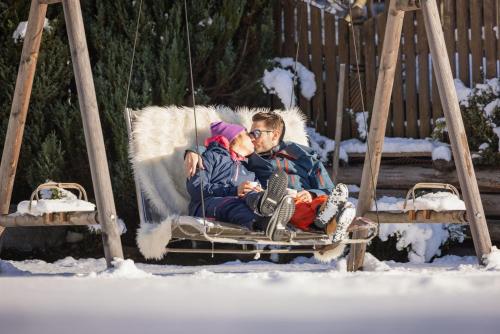 a man and a child sitting on a swing in the snow at Familien- & Vitalhotel Auenhof in Fulpmes