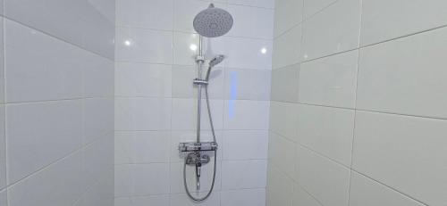 a shower with a shower head in a white tiled bathroom at Holi Homestay Trawas in Trawas