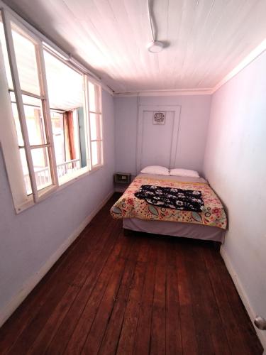 a small bedroom with a bed and two windows at Hostal Perro Watón in Valparaíso