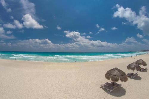 two umbrellas and chairs on a beach with the ocean at Sea Bloom in Cancún