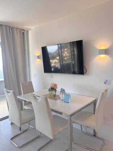 a dining room table with white chairs and a tv on the wall at SARA RIVIERA Costa Plana in Cap d'Ail