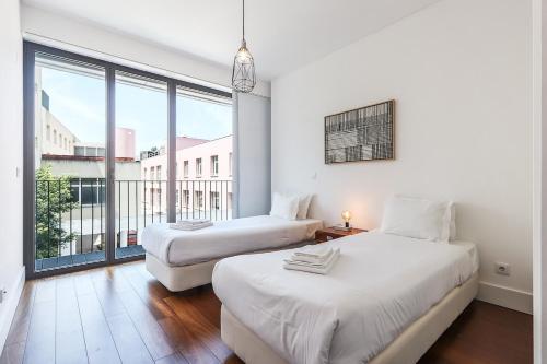 two beds in a room with a large window at Alcantara Lovely With Balcony 2 Bdr Apt with AC in Lisbon