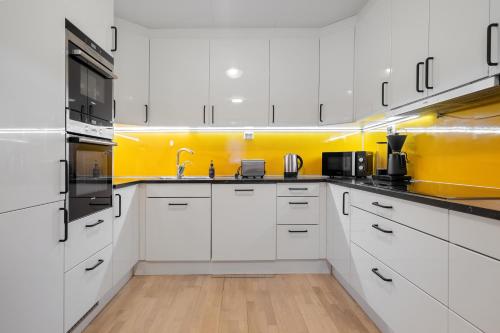 a kitchen with white cabinets and a yellow wall at Near Downtown - Large Beds - Free Parking in Tromsø