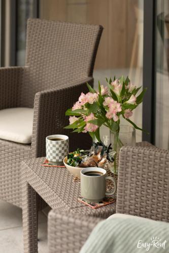a table with a vase of flowers and two cups at K&K Apartment - Premium z basenem - SeaShell - Easy - Rent Apartments in Łukęcin