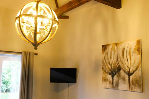 a chandelier hanging from a wall with a painting and a television at Beautiful Cotswold Couples Retreat in Bourton on the Water