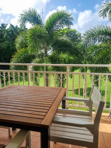 a wooden table and chair on a balcony with palm trees at Studio Premium piscine et bord de mer in Sainte-Luce