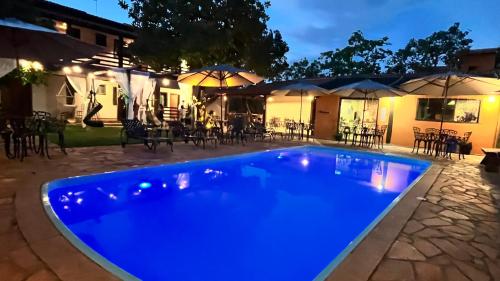 a blue swimming pool at night with tables and umbrellas at Pousada Flor de Pequi in Serra do Cipo