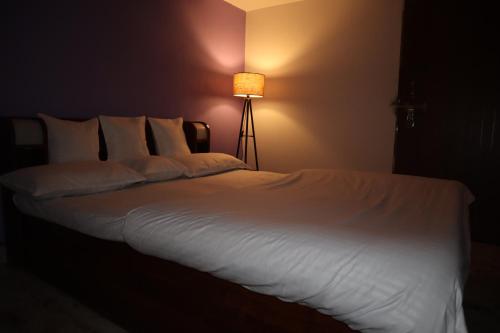 a bed with white sheets and a lamp in a room at The Kumbh Comfort Homestay in Prayagraj