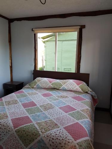 a bed with a quilt on it with a window at Turismo Raíces in Coihaique