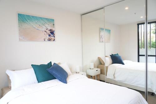a white bedroom with two beds and a mirror at St Kilda Fitzroy St apt in secure luxury building in Melbourne