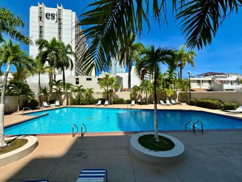 - une piscine avec un palmier et des bâtiments dans l'établissement Downtown Isla Verde Luxe Apartment with Pool, à San Juan