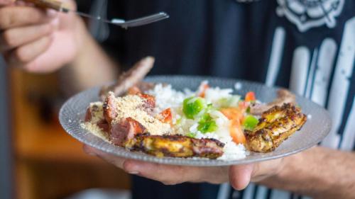 a person holding a plate of food with rice and meat at CASA 51 HOSTEL ubatuba in Ubatuba