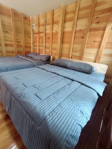 two beds in a bedroom with a wooden wall at อินทนนท์สุขุมทิพย์ โฮมสเตย์ in Ban Yang