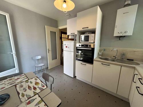 une cuisine avec des armoires blanches, une table et un évier dans l'établissement Maison cosy près plage avec jardin et parking - FR-1-224C-332, à Saint-Jean-de-Monts