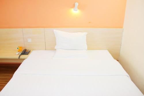a white bed in a room with a light on the wall at 7Days Inn Chengdu Chengyu Interchange Station in Chengdu