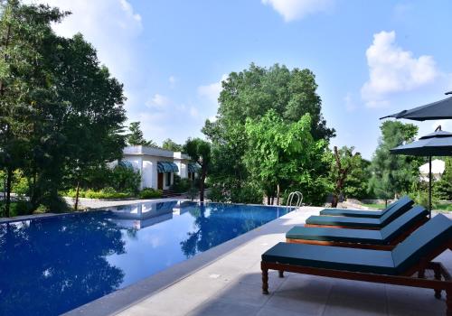 a pool with two lounge chairs and an umbrella at Clarks Safari Ranthambore in Khilchipur