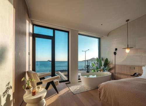 a bedroom with a bed and a bath tub and the ocean at Qingdao Wushe Yujianshanju Tangchi Seaview Hotel in Qingdao