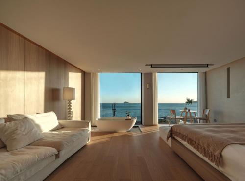 a bedroom with a bed and a bath tub and the ocean at Qingdao Wushe Yujianshanju Tangchi Seaview Hotel in Qingdao
