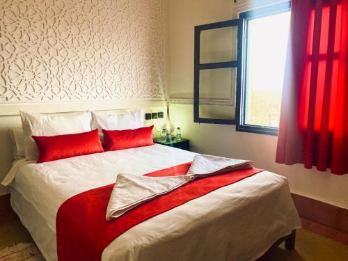 a bedroom with a bed with red pillows and a window at Hotel Kasbah Ennakhile in Nkob