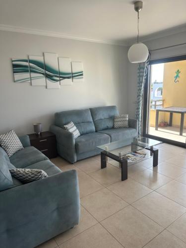 a living room with a blue couch and a glass table at Jardins da guia in Albufeira