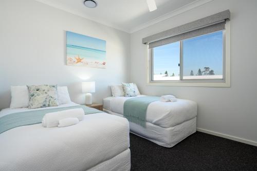 a white bedroom with two beds and a window at Casablanca Luxury Retreat near Shellharbour Marina in Shellharbour