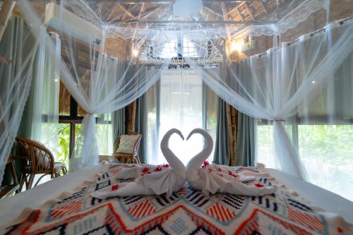 a bedroom with a bed with a swan making a heart at Inigtan Lio Bamboo Cottages in El Nido