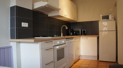 - une cuisine avec des appareils électroménagers blancs et des murs en carrelage noir dans l'établissement Gîte Jardin - LA FERME TRANQUILLE, à Puivert