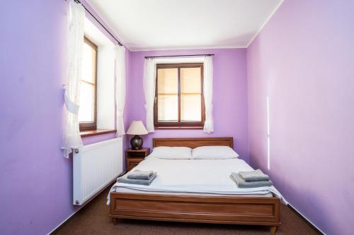 a purple bedroom with a bed and two windows at Penzion Fialka in Velké Losiny