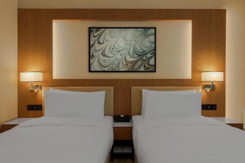 two beds in a hotel room with a painting on the wall at Millennium Al Masar in Jeddah