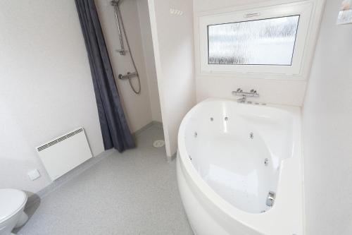 La salle de bains blanche est pourvue d'une baignoire et d'une fenêtre. dans l'établissement First Camp Bøjden Strand, à Fåborg