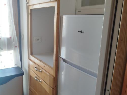 La cuisine est équipée d'un réfrigérateur blanc et d'une armoire en bois. dans l'établissement Appartement de 2 pièces exposé Sud/Ouest avec balcon et vue montagnes à Tignes - FR-1-449-185, à Tignes