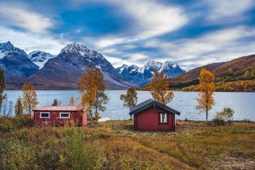 two houses on the shore of a lake with mountains at Traditional Arctic Farmhouse in Sørlenangen