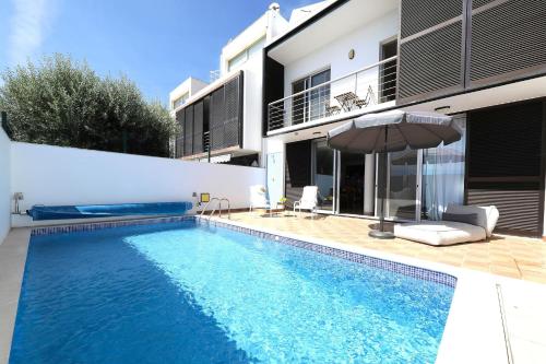 a swimming pool with an umbrella next to a house at Casa Frangipani, Quinta da Foz in Tavira