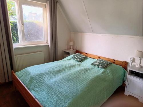 a bedroom with a bed with a green comforter and a window at Cozy holiday home in Sint Maartenszee in Sint Maartenszee