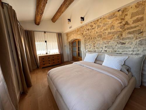 - un grand lit dans une chambre dotée d'un mur en pierre dans l'établissement Le Mas du Mas d' Antonegre, à Montbazin