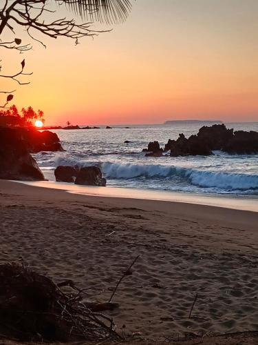 a sunset on a beach with rocks in the ocean at Los Paniquines Ecolodge in Drake