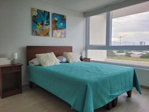ein Schlafzimmer mit einem Bett mit einer blauen Decke und einem Fenster in der Unterkunft Departamento Laguna del Mar in La Serena