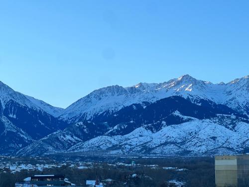 a snow covered mountain range with a town in front at Banur Ип in Almaty