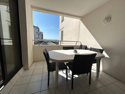 d'une table et de chaises blanches sur un balcon avec fenêtre. dans l'établissement T3 rénové avec piscine et parking au Cap d'Agde - FR-1-749-79, au Cap d'Agde