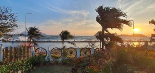 a sunset on the beach with a fence and palm trees at SeeSea Thai wooden house on beachfront in Prachuap Khiri Khan