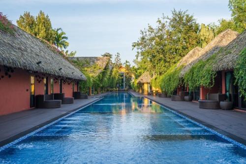 a swimming pool in a resort with thatched roofs at Khum Damnoen Resort in Ratchaburi
