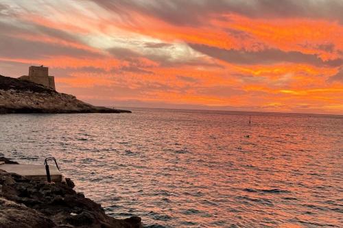 a sunset over a body of water with a building at Gozo Xlendi Coastal Apartment with Stunning Sea View, Free Private Parking, AC & WiFi in Xlendi