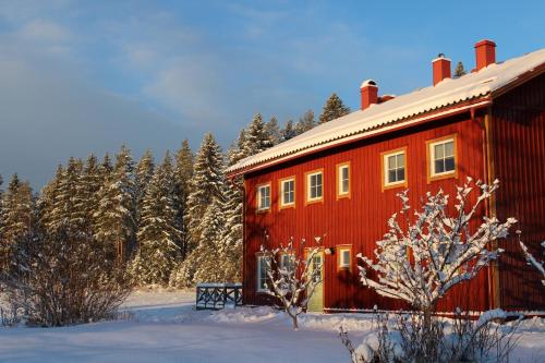 a red barn in the snow next to trees at Allsta Gård Kretsloppshuset B&B in Bjärtrå