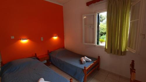 two beds in a room with orange walls and a window at Dimitris Studios in Paleokastritsa