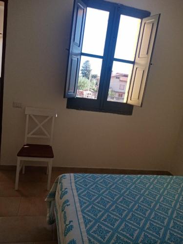 a bedroom with a bed and a window and a chair at Su Furriadroxiu in San Vito