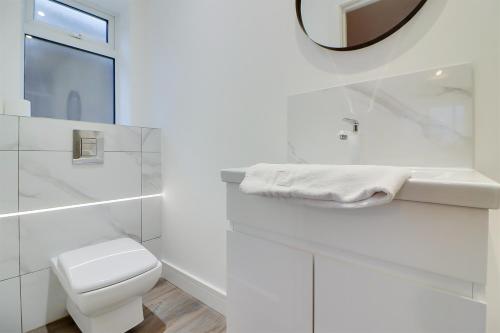 a white bathroom with a toilet and a mirror at Spacious 5-Bedroom Home, Sleeps 9, Near Hospital with Driveway Parking in Peterborough
