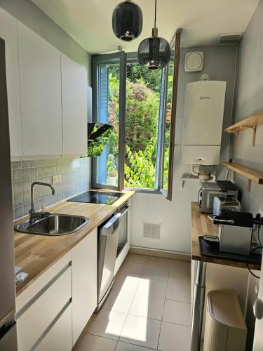 une cuisine avec des armoires blanches, un évier et une fenêtre dans l'établissement Charmant 3 pièces Rueil Malmaison cœur de ville, à Rueil-Malmaison