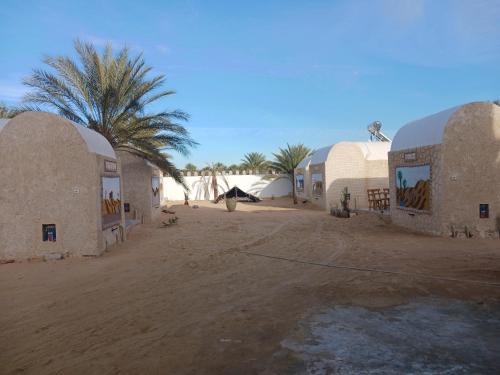 a group of buildings in the desert with a palm tree at Maisons la Porte de Désert à Douz in Douz