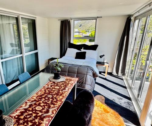 a bedroom with a bed and a table and windows at Airport Guesthouse in Queenstown